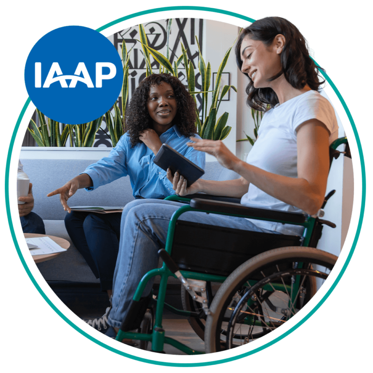 Two women having a discussion, one seated in a wheelchair holding a tablet.